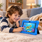 A young boy with brown hair lies on a cream carpet in a cozy living room, smiling at a colorful underwater cartoon screen on a blue protective Learning tablet.