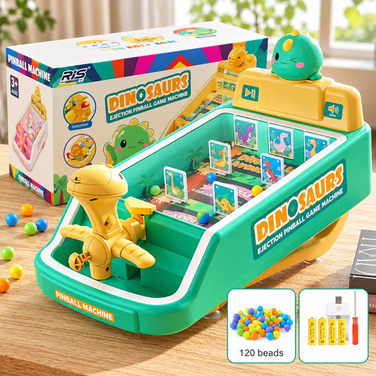 A children's tabletop pinball machine labeled 'DINOSAURS' with a green and yellow plastic body, a dinosaur-shaped pinball target, scoring display, and retail box shown behind it. The scene includes a wooden tabletop and a blurred real-world background, so this is Lifestyle rather than Product/Packaging.
