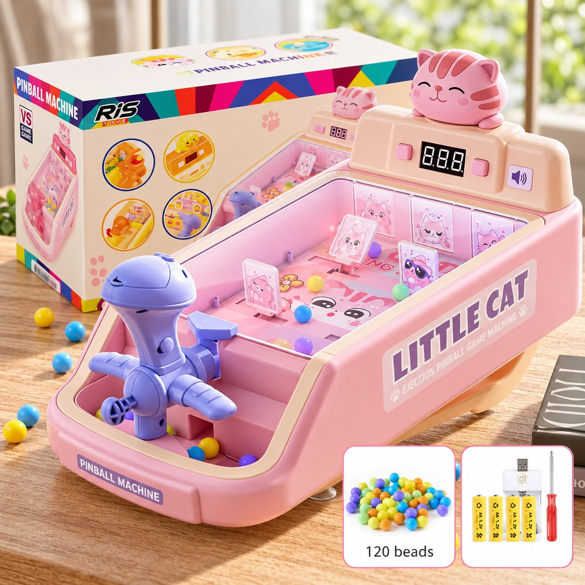 Pink rechargeable tabletop pinball machine toy labeled 'LITTLE CAT' with a cat face display, small ball bins, a blue robotic claw, and accessories including beads and batteries. The product is shown with its retail box on a tabletop.

